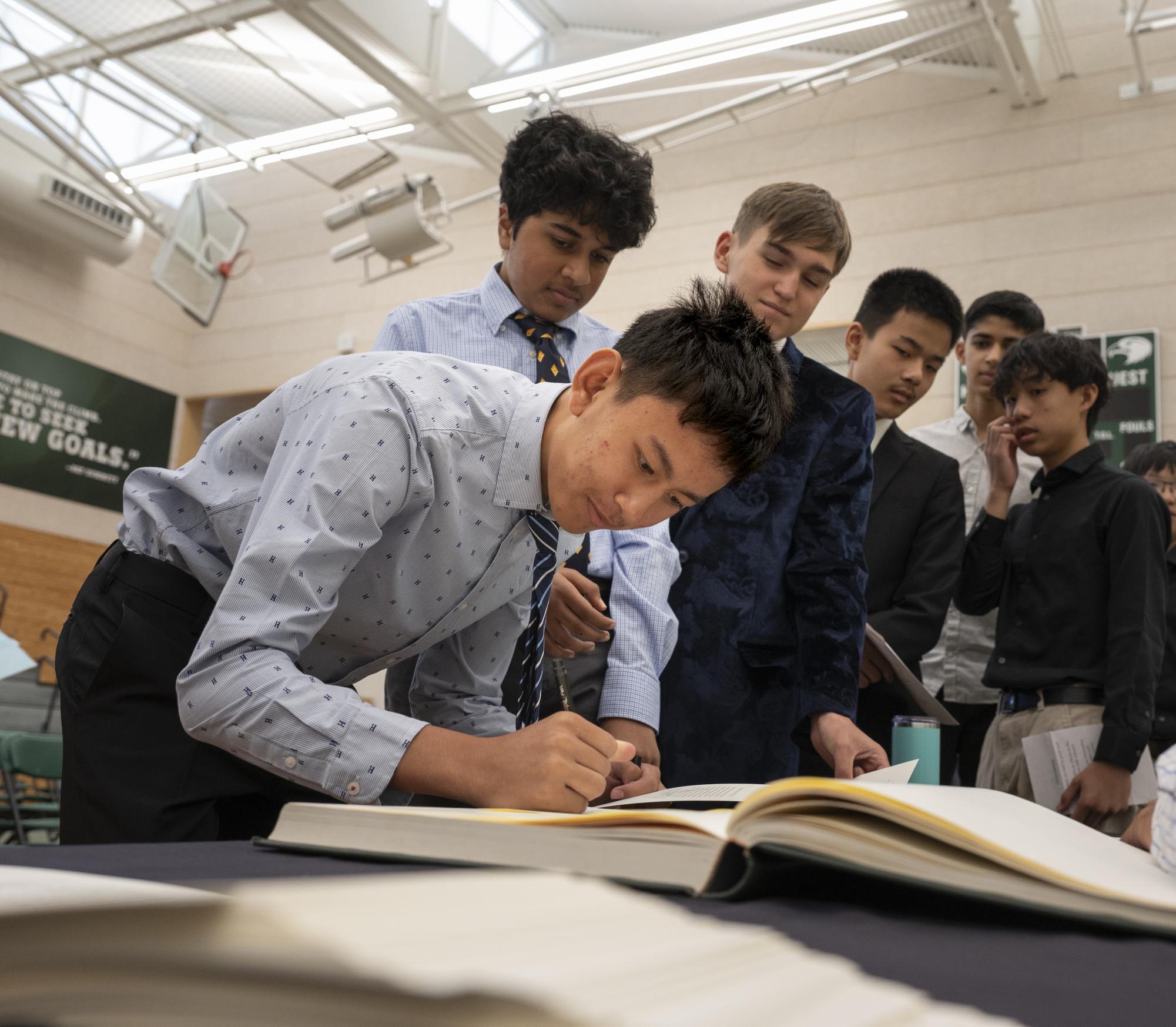 Alvin Siamwalla (9) signs the Matriculation book as other frosh watch. Before signing, the whole school read the Matriculation Oath together.