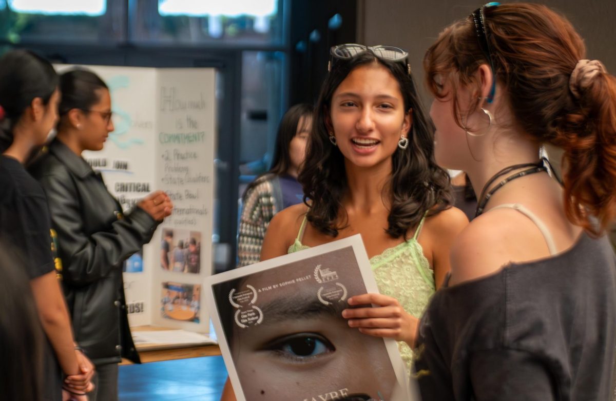 Sophie Pellet (11) introduces Film Club to Avanya Glass (12), holding poster of last school years short film production “Maybe Next Time.” Film Club decorated their board with fairy lights and photos.