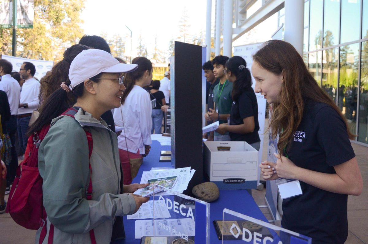 Business program representative Nicole Dean (10) sums up the DECA program for a parent during Back to School Day on Saturday morning. DECA was one of the many upper school programs and organizations represented by booths in front of the RPAC.