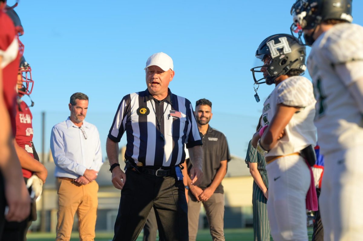 A referee from Bay Area Sports Officials speaks to the varsity football captains from Harker and Anzar before the coin toss of the Homecoming game. BASO supplies most referees for Harker but lost over 50% of their referees after the COVID-19 pandemic. 