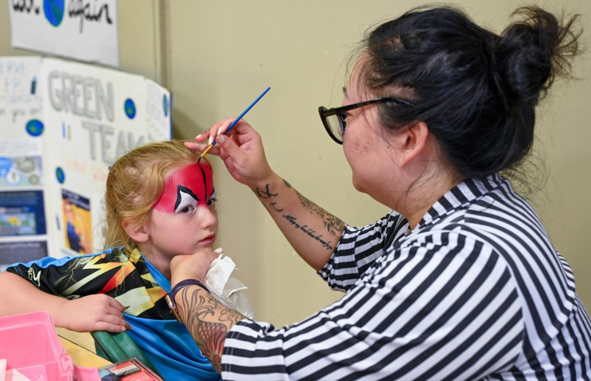 A face painting artist draws a design on a Harker Day attendee's forehead. Students and parents also had the opportunity to receive a caricature of themselves in the Quad.