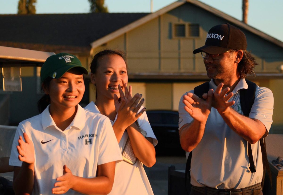 To support their teammates, varsity girls golf players Sai Kaneshiro (9) and Joyce He (10) clap alongside assistant coach Sean Tamashiro. "The girls encourage each other, and there's a lot of support within the team," Tamashiro said.