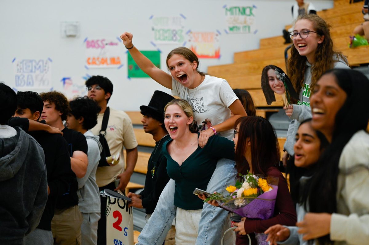 Senior Claire Anderson rides on senior Kylie Anderson's back, cheering after the varsity girls volleyball team won their game. The last regular season home game drew a large audience of students, staff and parents. 