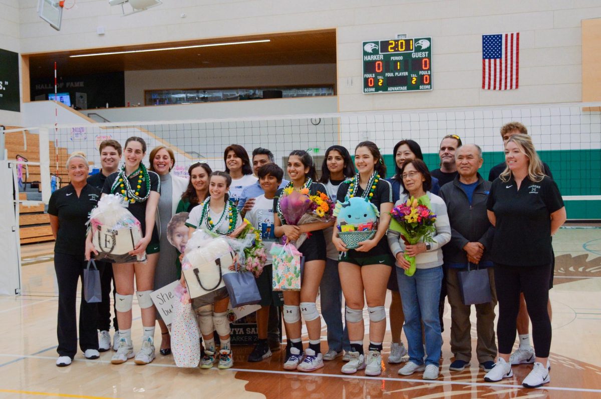 Varsity girls volleyball seniors Emily Mitnick, Norah Mehanna, Navya Samuel and Stephanie Bossalina hold bouquets and gifts while smiling for a photo with family members and coaches.  “Although it's our last moment on this court as seniors and it's bittersweet, I've had great memories this season," Stephanie said. 