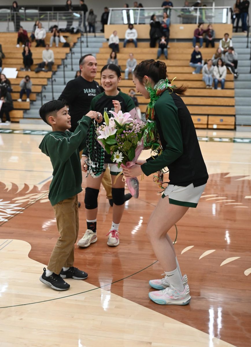 Senior Gemma Chan stoops down to receive a bouquet of flowers from Assistant Coach Kiira Rodriguez's son. As each senior received gifts, head coach Daniza Rodriguez read aloud a short speech that each senior wrote about their time playing for Harker.