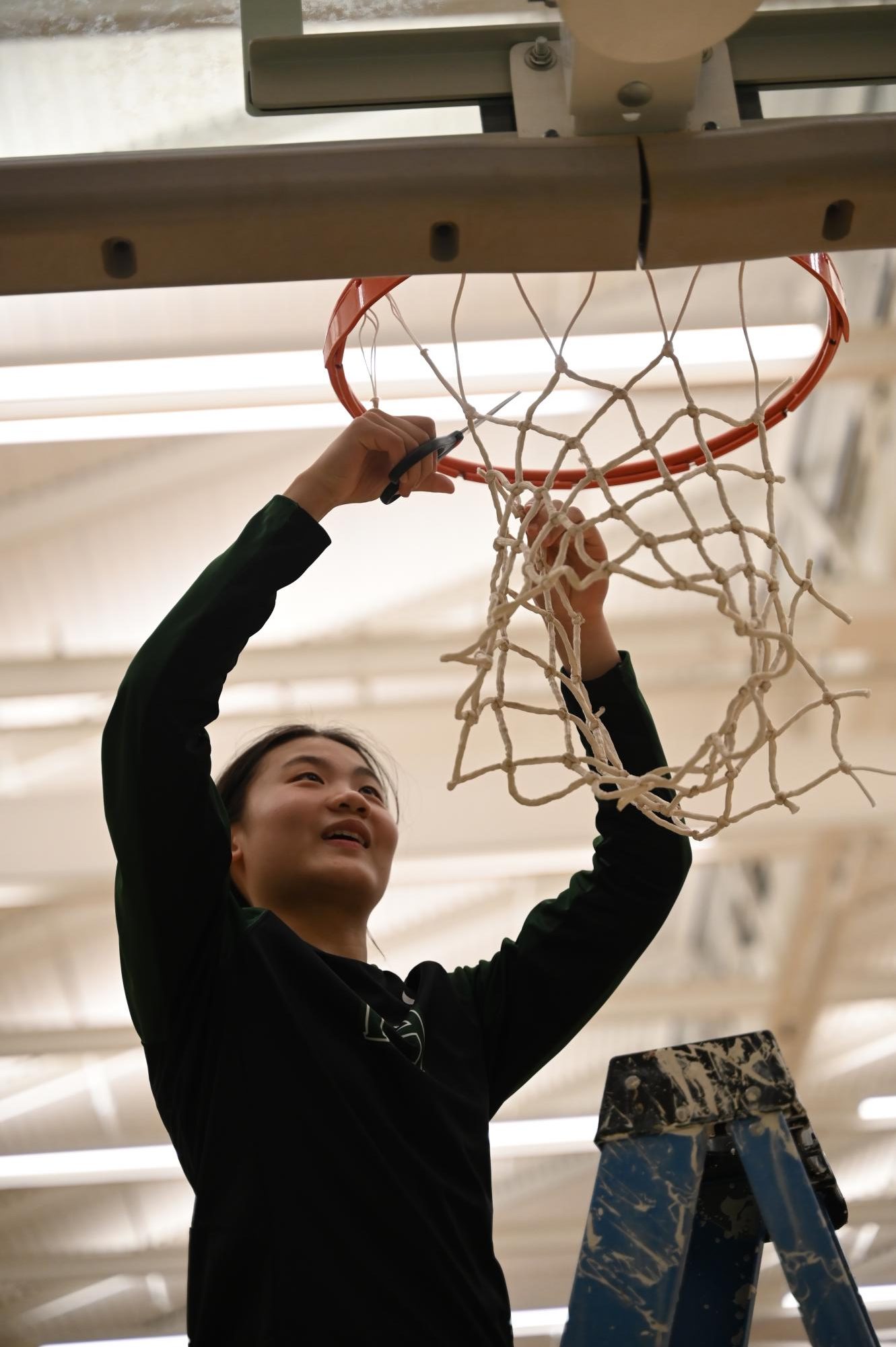 Point guard Jillian Chen (9) uses scissors to cut off a section of the basketball net. On senior night, every member of the team received a piece of the net to commemorate their last home game of the season.