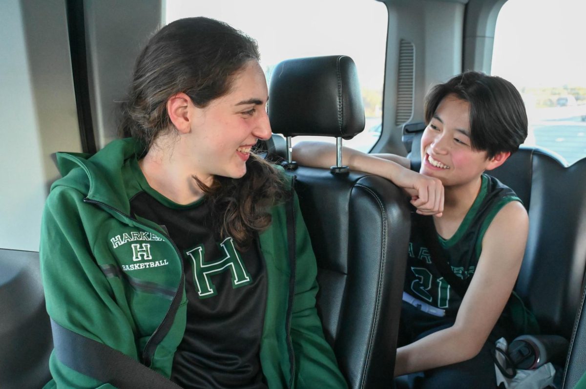 Varsity girls basketball player Finley Ho (10) leans over the seat to talk to captain Emily Mitnick (12). On the bus ride to games, teammates share snacks and trade stories, taking the opportunity to grow closer off the court.