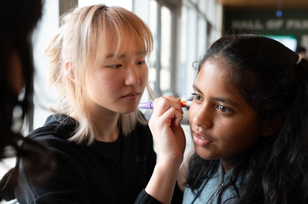 Junior Mia Tang draws on her Eagle Buddy's face with an orange pen. After the People's Circus Theatre performed, juniors and fourth graders rotated to three stations: face painting, scarf juggling, and feather balancing.