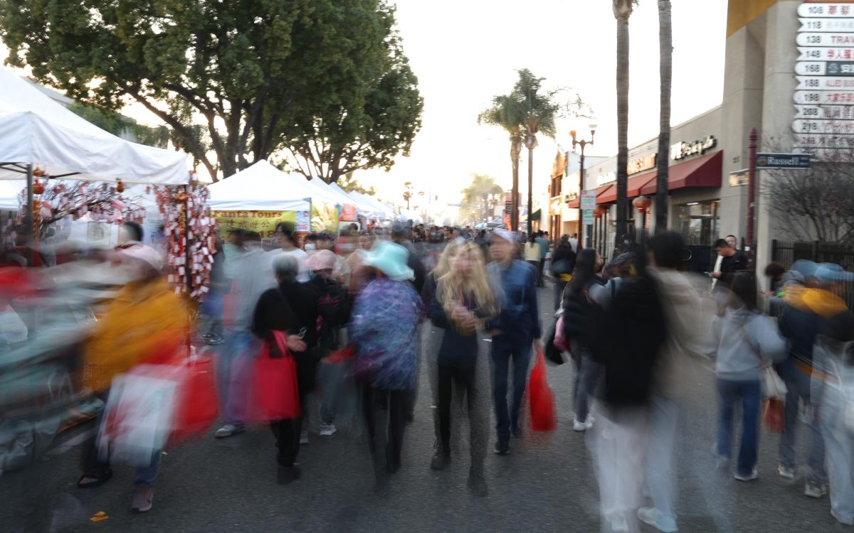 People stroll through Chinatown during a day lunar new year celebration. Street vendors display their goods and red decorations hang from the windows of many shops.