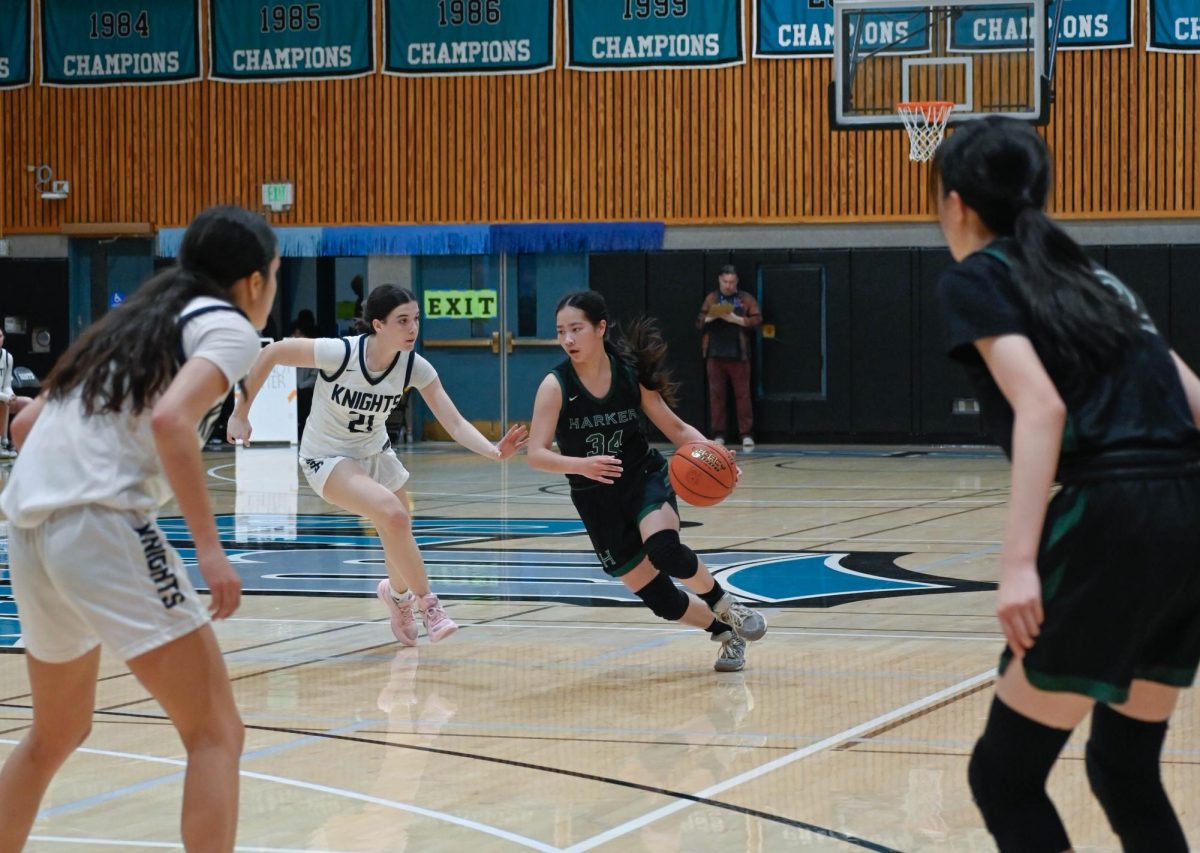 Guard Isabella Lo (12) evades Knights players as she carries the ball down the center of the court. While Harker created numerous opportunities for layups and shots, Menlo capitalized on free throws, allowing them to overtake the Eagles.