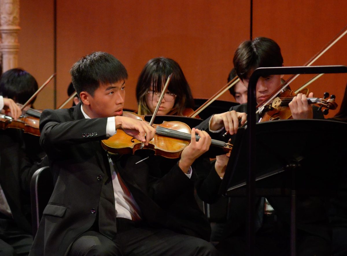 Junior concertmaster George Yang looks at the sheet music as he draws his bow. The orchestra and jazz band played nine pieces during the concert.