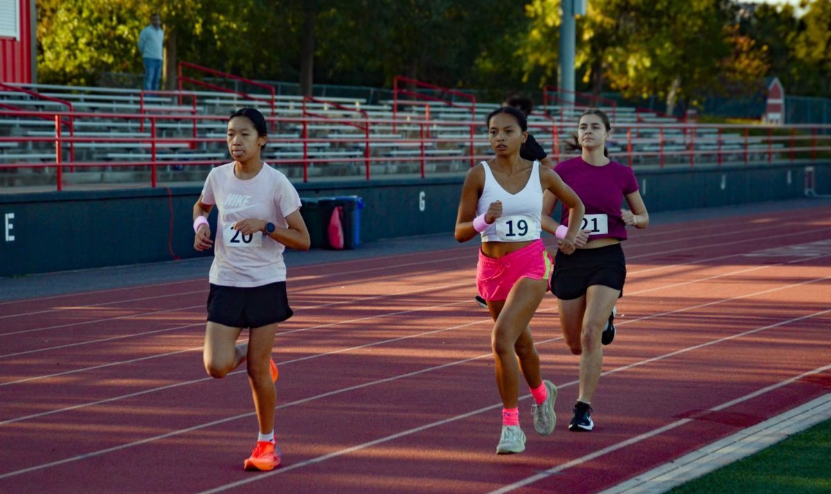 Sophie Shen (9), Ava Alvarez (11) and Emily Bryan (12) race at the Gunn High School track during the 2-mile Hoka Postals. Runners completed eight laps around the track.
