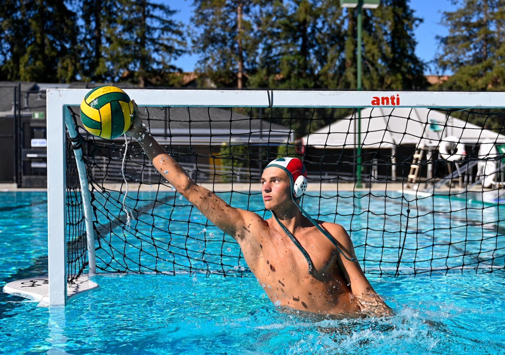 Varsity boys water polo goalie Alejandro Cheline (12) reaches up to block a shot from the cage. When competing in the 18U Platinum Division, Alejandro held the national record of 9.8 blocks per game. 
