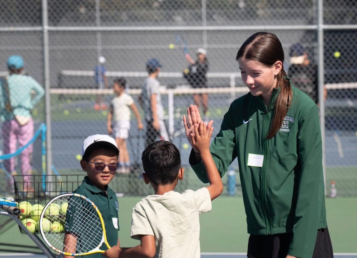 Varsity Tennis player Isabella Pop (10) high-fives a clinic attendee. She guided the young players in honing their forehand swing technique.