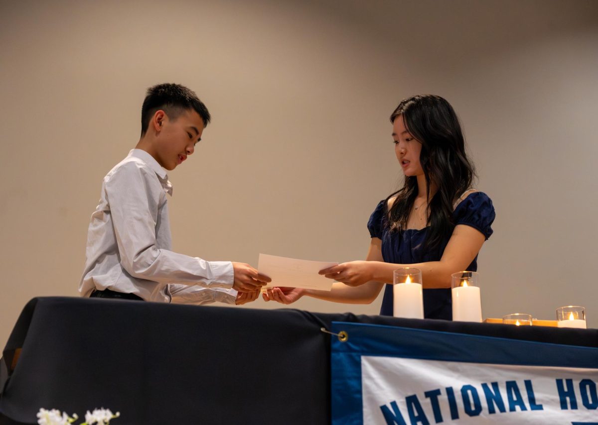 NHS Co-President Selina Wang (12) passes a signed certificate to inductee Lucas Lum (11). New NHS students were called to the auditorium stage during the final part of the ceremony to formalize their membership.