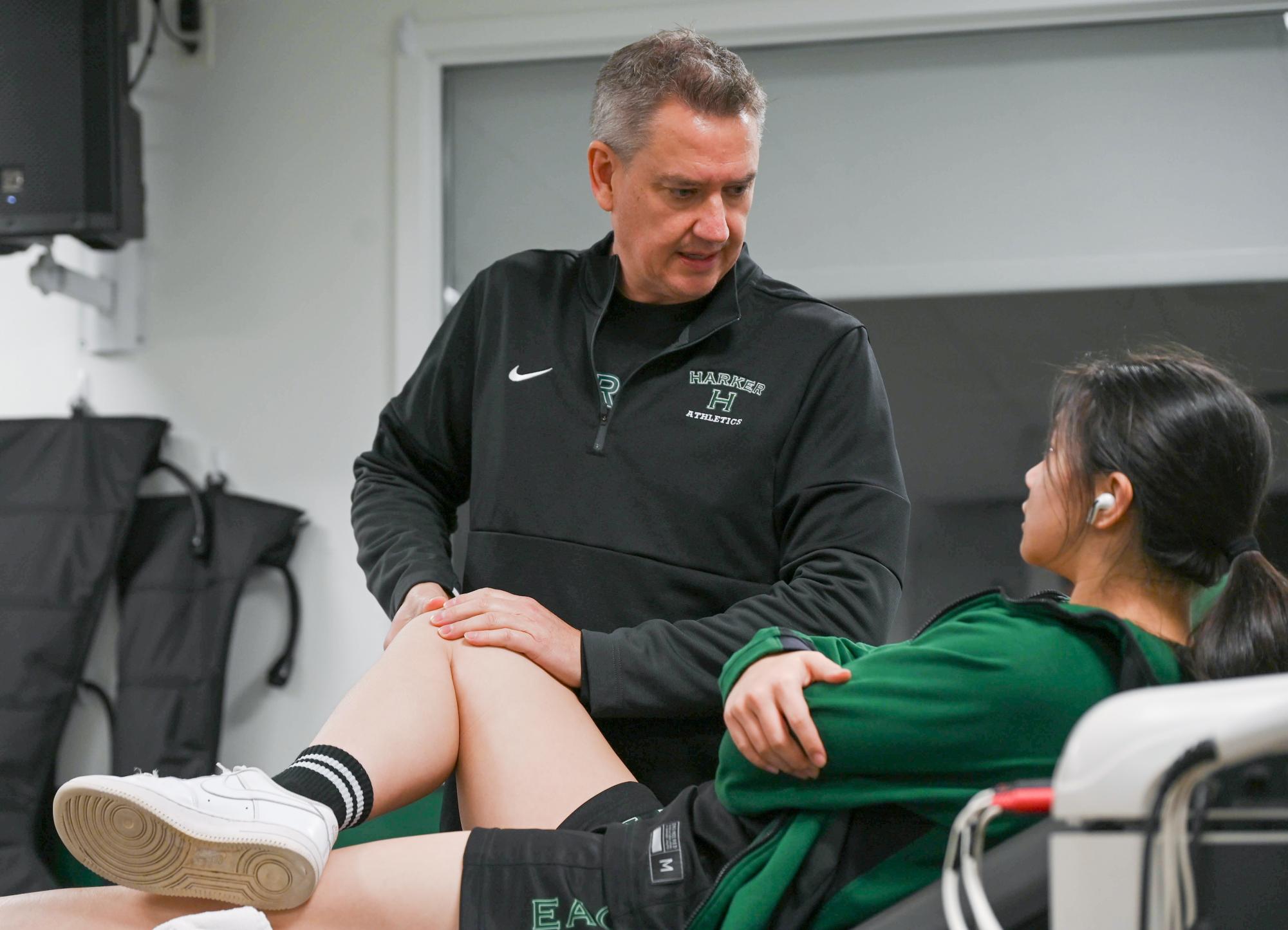 Athletic trainer Wes Howard assesses varsity girls basketball player Claire Yu (12)’s knee. The training room is available for all athletes to help with injury recovery.