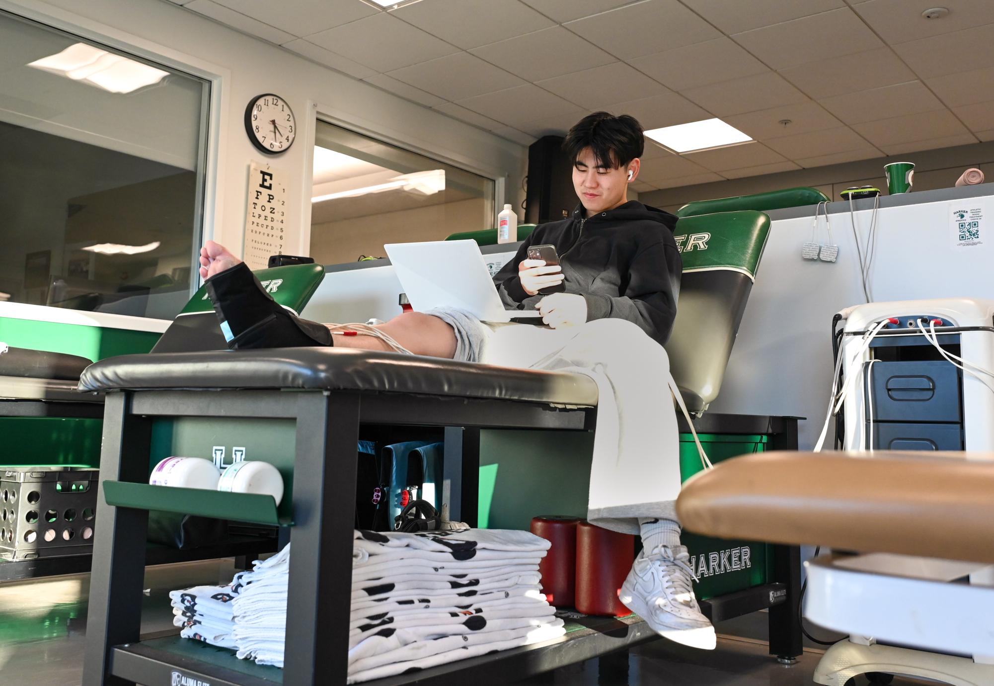 Varsity boys basketball player Alan Gao (12) studies while he receives interferential therapy at a taping station. Interferential therapy helps reduce swelling and relieve pain.