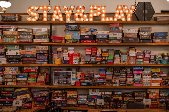 Rows of board games sit beneath a large “STAY & PLAY” sign inside Hex&Co., where visitors pay $15 per person for access to the collection.